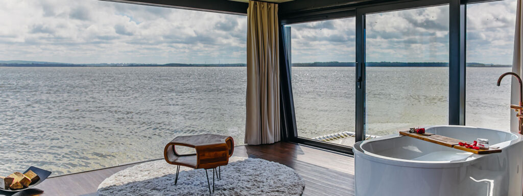 Nowoczesne wnętrze pływającego domku Houseboat z wanną, panoramicznymi oknami i widokiem na jezioro.