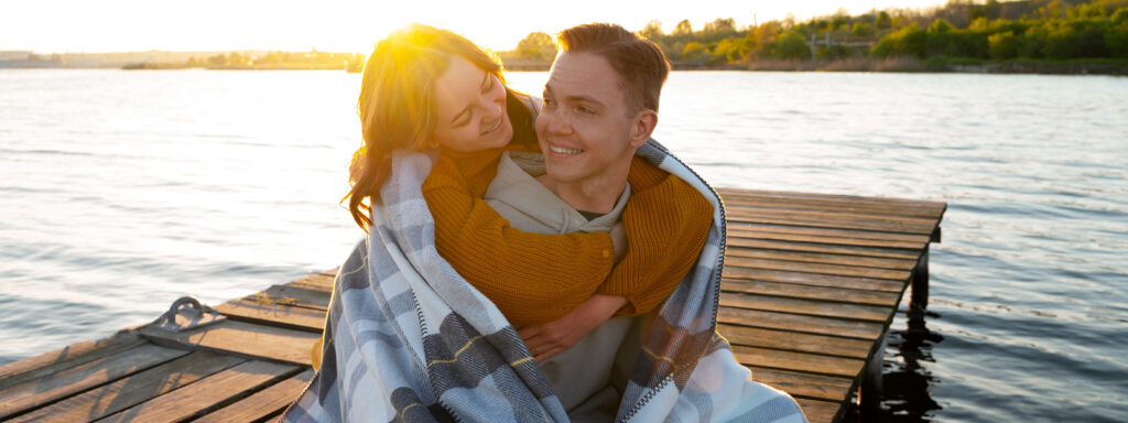 Para przytulająca się na pomoście nad jeziorem podczas zachodu słońca.