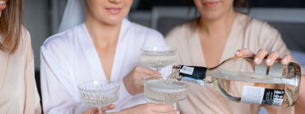 Grupa przyjaciółek w białych szlafrokach nalewające prosecco podczas wieczoru panieńskiego.